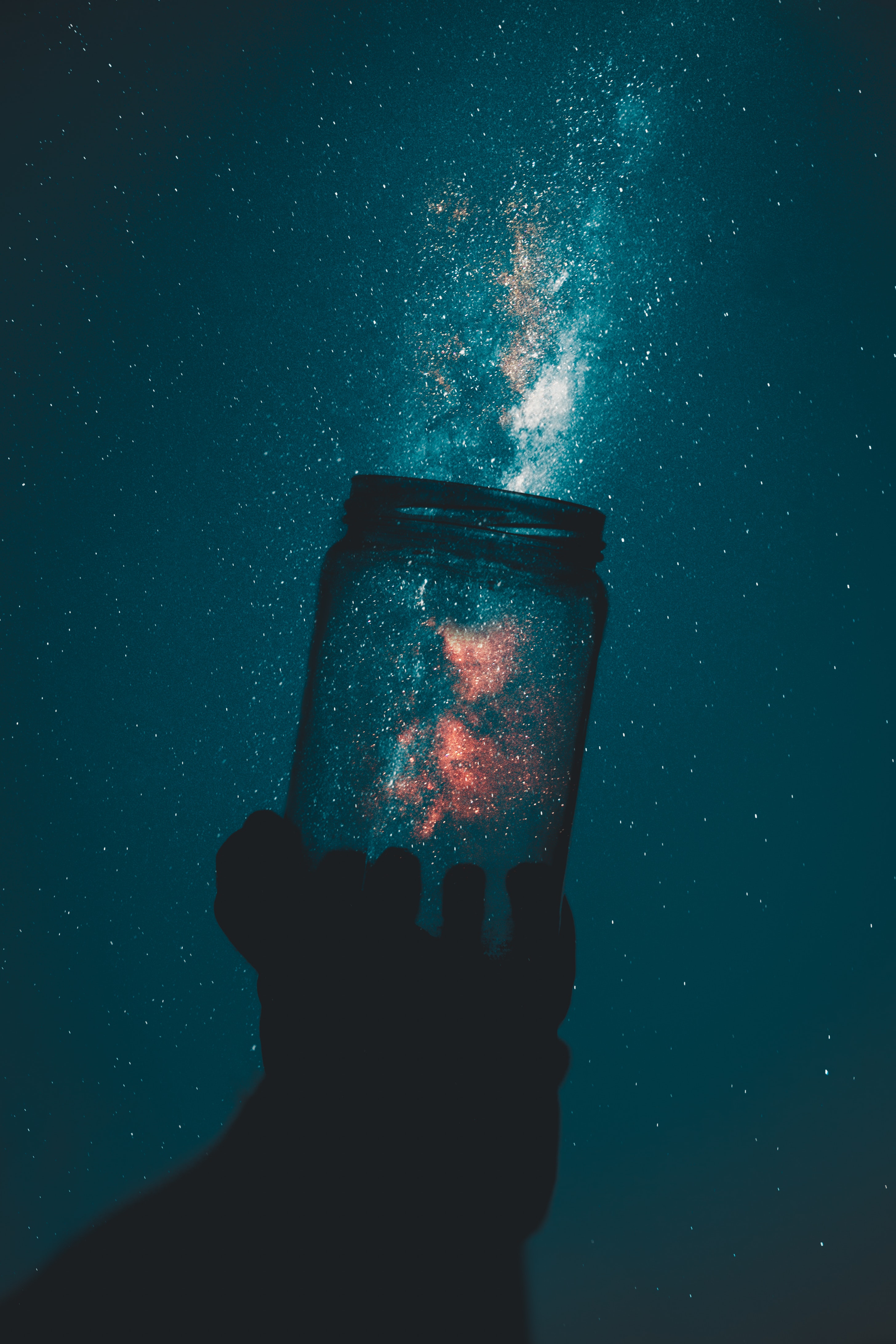 an optical illusion where a mason jar is held up to a starry night sky such that it looks like there are stars in the jar